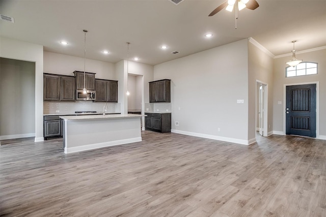 kitchen with pendant lighting, a high ceiling, hardwood / wood-style floors, decorative backsplash, and a kitchen island with sink