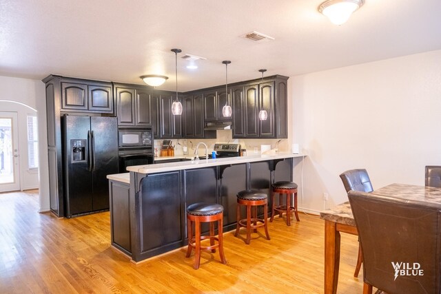 kitchen with a breakfast bar area, hanging light fixtures, kitchen peninsula, light hardwood / wood-style floors, and black appliances