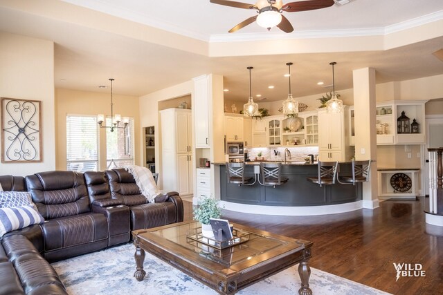 living room with ceiling fan with notable chandelier, dark wood-type flooring, and ornamental molding