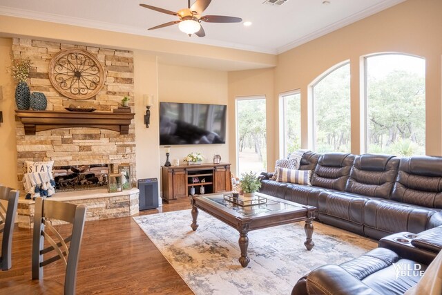 living room featuring hardwood / wood-style flooring, ornamental molding, a stone fireplace, and ceiling fan