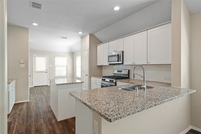 kitchen with dark wood-type flooring, stainless steel appliances, kitchen peninsula, and white cabinets