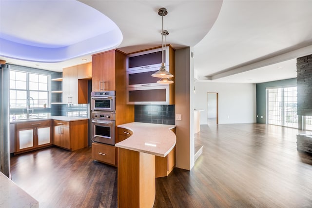 kitchen with pendant lighting, sink, double oven, dark hardwood / wood-style flooring, and kitchen peninsula