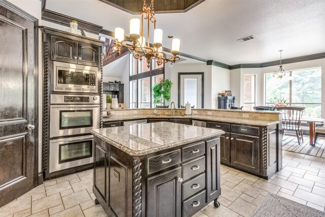 kitchen with a notable chandelier, crown molding, a kitchen island, light stone countertops, and appliances with stainless steel finishes