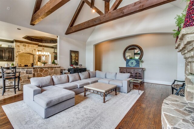 living room featuring a chandelier, beamed ceiling, dark hardwood / wood-style floors, a stone fireplace, and high vaulted ceiling