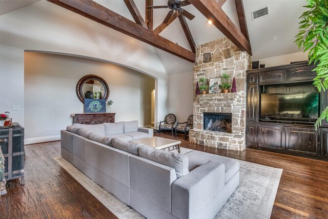 living room with dark hardwood / wood-style flooring, a stone fireplace, beam ceiling, high vaulted ceiling, and ceiling fan