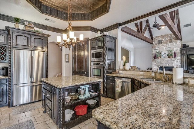 kitchen with a fireplace, a center island, ceiling fan with notable chandelier, light stone countertops, and stainless steel appliances