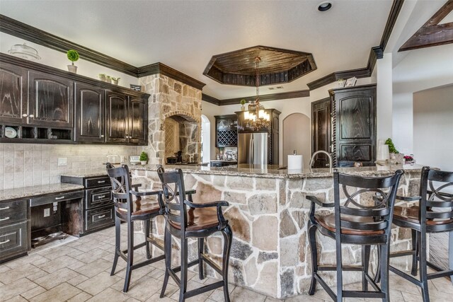 kitchen with light stone counters, a chandelier, stainless steel refrigerator, kitchen peninsula, and a breakfast bar