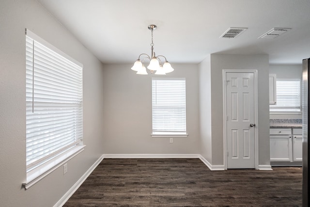 unfurnished room with a wealth of natural light, dark wood-type flooring, and an inviting chandelier