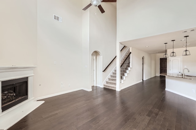 unfurnished living room with a towering ceiling, dark hardwood / wood-style flooring, ceiling fan, and sink