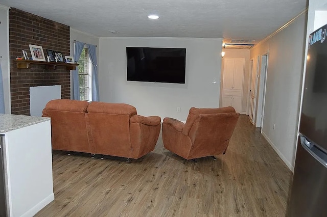 living room with a textured ceiling, crown molding, light wood-type flooring, and a fireplace