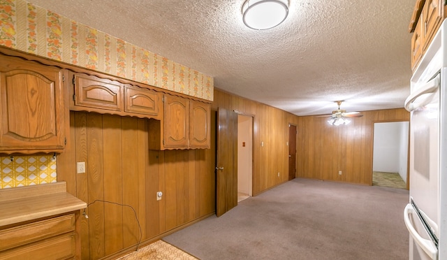 interior space with a textured ceiling, light colored carpet, ceiling fan, and wood walls