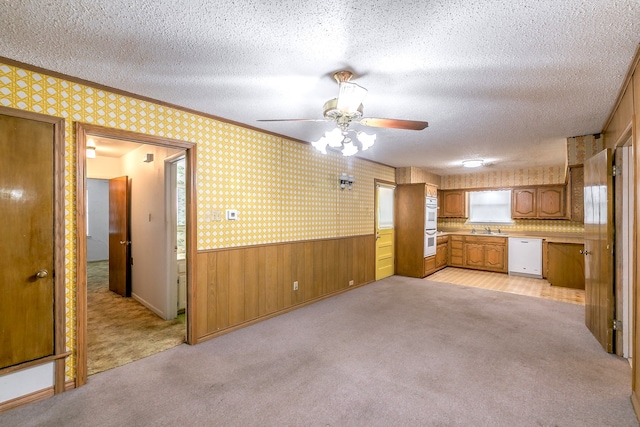 unfurnished living room featuring a textured ceiling, ceiling fan, light carpet, and wooden walls