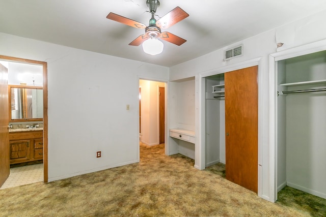 unfurnished bedroom featuring multiple closets, ensuite bath, light carpet, sink, and ceiling fan