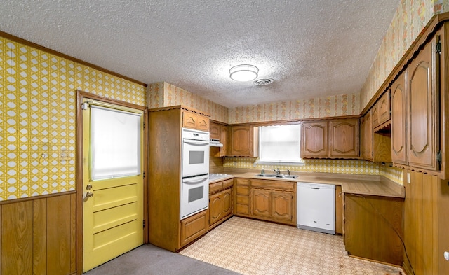 kitchen featuring wooden walls, crown molding, white appliances, sink, and a textured ceiling