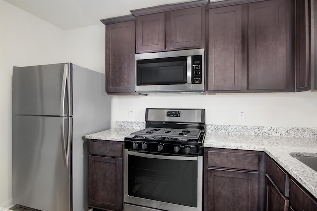 kitchen with appliances with stainless steel finishes, light stone counters, and dark brown cabinetry