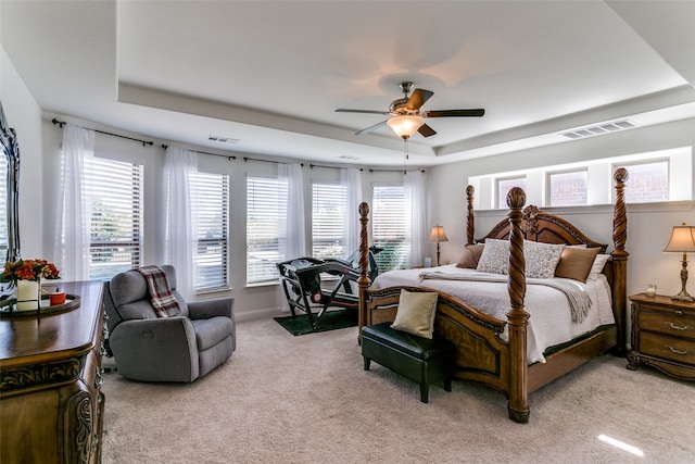 bedroom with ceiling fan, light carpet, a tray ceiling, and multiple windows