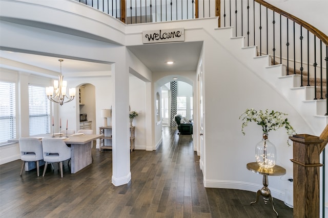 foyer entrance with dark hardwood / wood-style floors, a towering ceiling, a wealth of natural light, and a chandelier