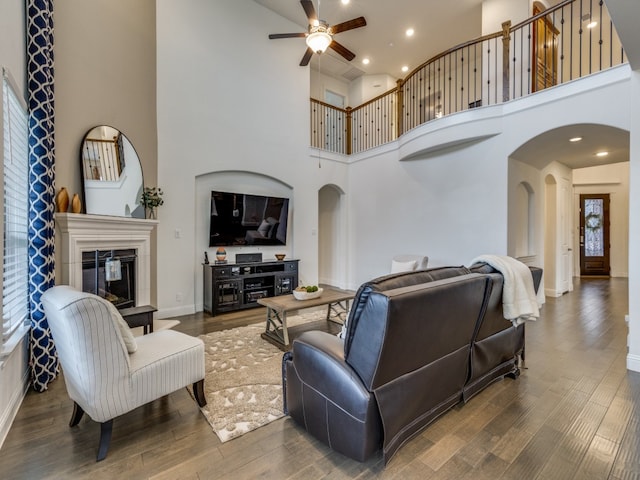 living room with ceiling fan, a towering ceiling, and hardwood / wood-style flooring