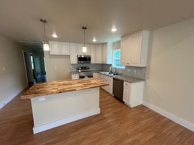 kitchen with butcher block counters, a center island, stainless steel appliances, pendant lighting, and white cabinets