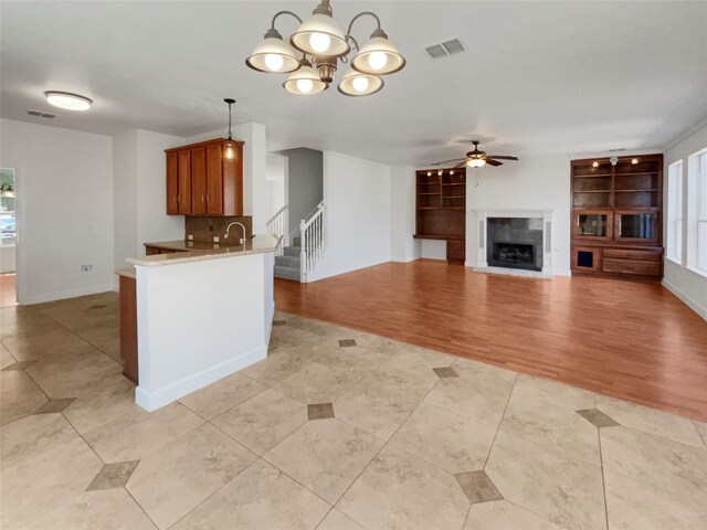 kitchen with ceiling fan with notable chandelier, pendant lighting, light hardwood / wood-style floors, kitchen peninsula, and sink