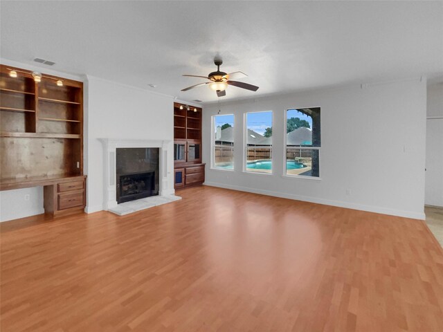 unfurnished living room with built in features, ceiling fan, a tile fireplace, and hardwood / wood-style flooring