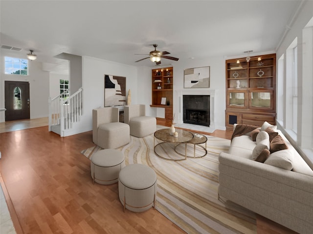 living room with a premium fireplace, built in features, and light hardwood / wood-style floors