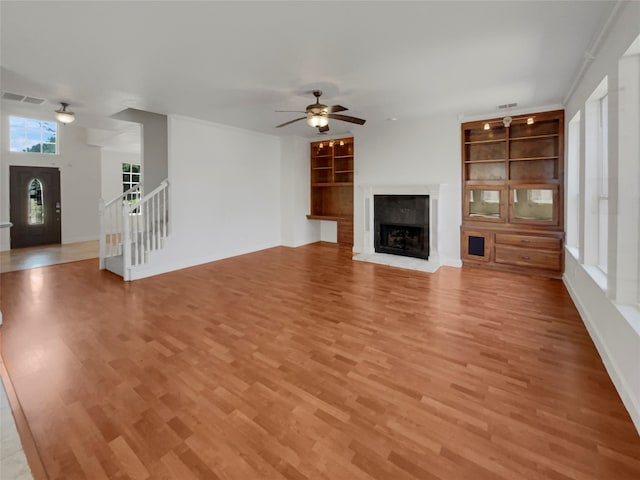 unfurnished living room with built in features, ceiling fan, and hardwood / wood-style flooring