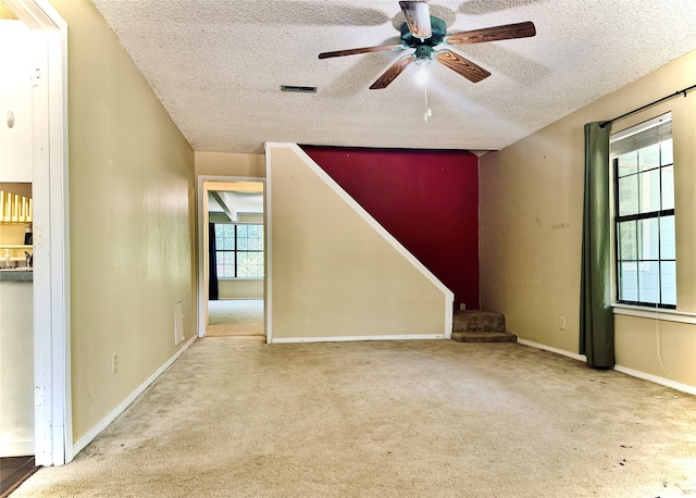 unfurnished room with a textured ceiling, ceiling fan, and light carpet