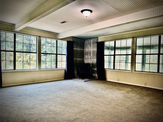 unfurnished living room featuring a wood stove, plenty of natural light, carpet flooring, and wood walls