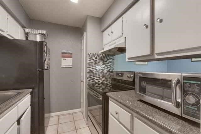 kitchen featuring decorative backsplash, freestanding refrigerator, white cabinetry, stainless steel range with electric stovetop, and under cabinet range hood