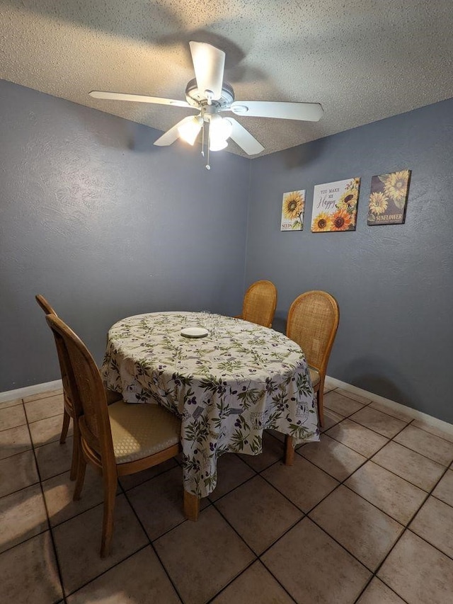 tiled dining space with ceiling fan, a textured ceiling, and baseboards