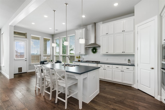 kitchen featuring an island with sink, pendant lighting, wall chimney exhaust hood, and white cabinetry