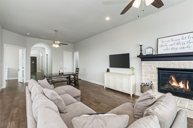 living room with dark wood-type flooring, ceiling fan, and a stone fireplace