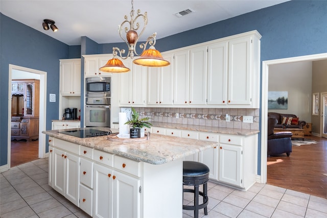 kitchen with tasteful backsplash, a kitchen island, appliances with stainless steel finishes, white cabinets, and light hardwood / wood-style floors