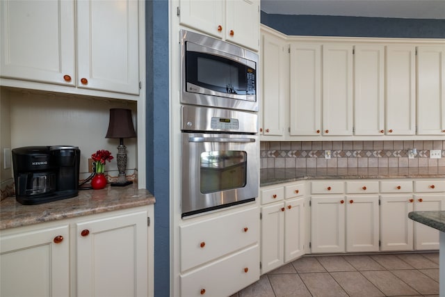 kitchen featuring backsplash, appliances with stainless steel finishes, stone countertops, white cabinetry, and light tile patterned flooring