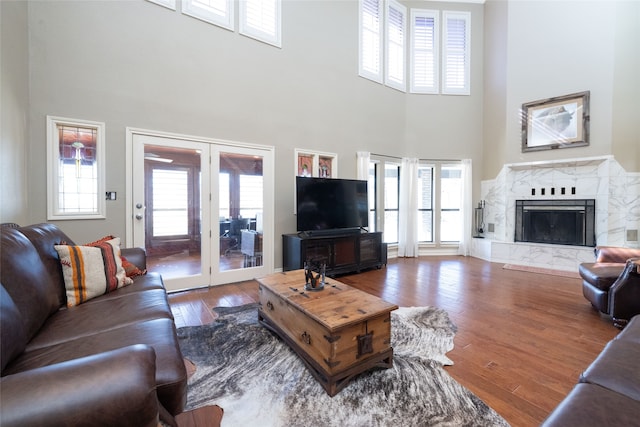 living room with french doors, hardwood / wood-style floors, a high ceiling, and a premium fireplace