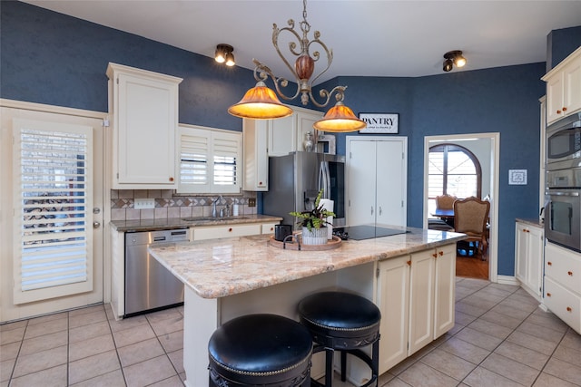 kitchen with a kitchen island, appliances with stainless steel finishes, sink, light stone counters, and white cabinets