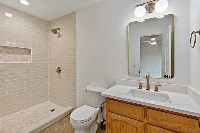 bathroom with tile patterned flooring, tiled shower, ceiling fan, vanity, and toilet