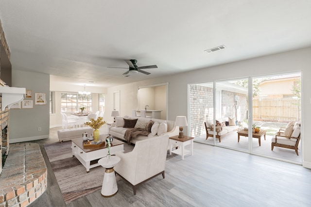 living room featuring a brick fireplace, hardwood / wood-style flooring, and ceiling fan with notable chandelier