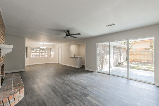 unfurnished living room with ceiling fan with notable chandelier, dark wood-type flooring, and a fireplace