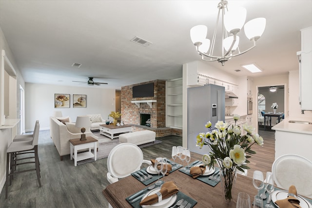 dining area featuring ceiling fan with notable chandelier, dark wood-type flooring, and a fireplace