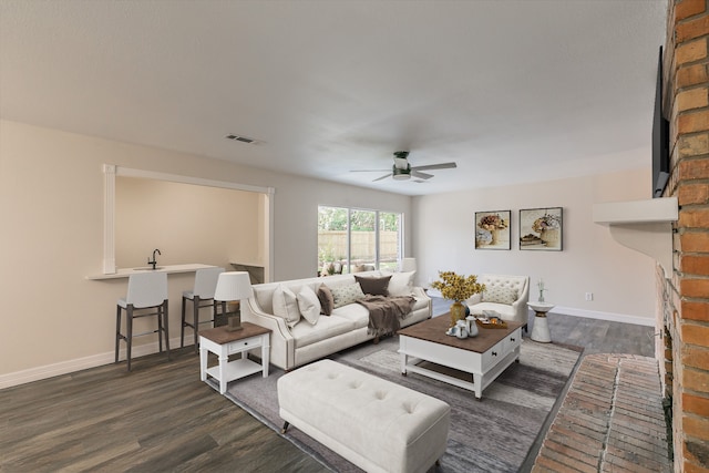 living room with a brick fireplace, dark wood-type flooring, and ceiling fan