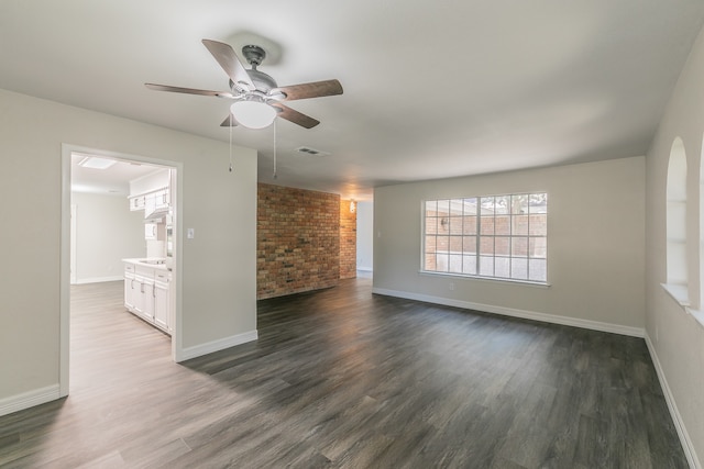 unfurnished living room with ceiling fan, brick wall, and dark hardwood / wood-style floors