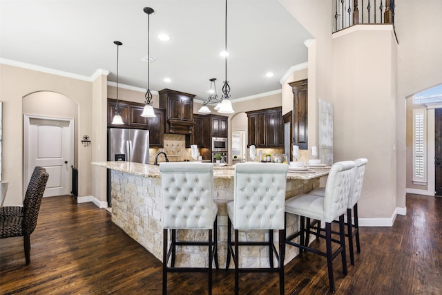 kitchen with light stone counters, stainless steel appliances, decorative light fixtures, and dark brown cabinets