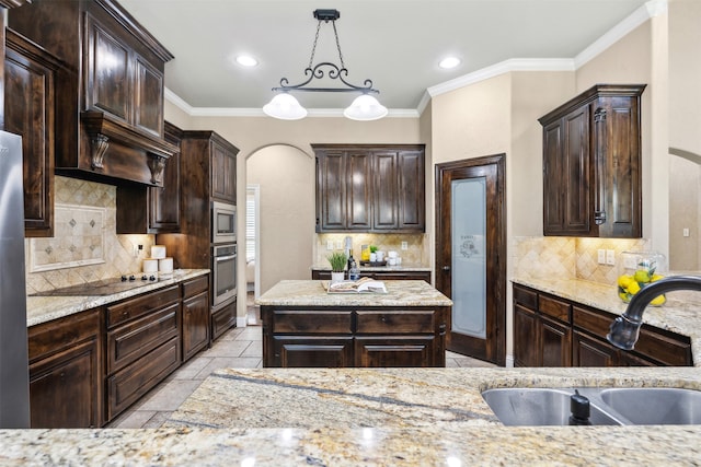 kitchen with pendant lighting, sink, appliances with stainless steel finishes, dark brown cabinets, and light stone counters