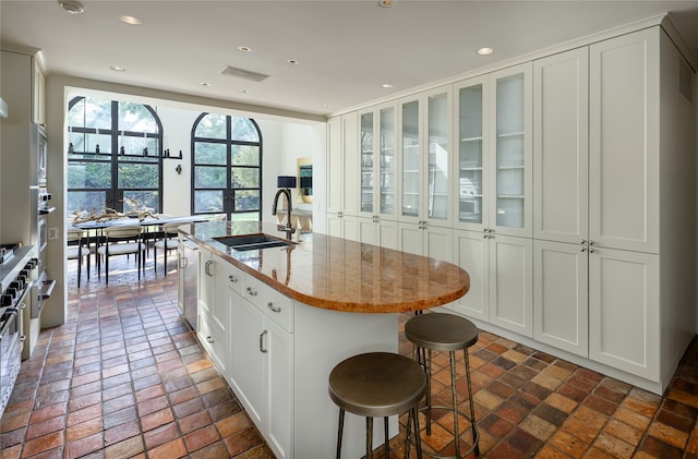 kitchen with white cabinetry, a kitchen bar, light stone counters, sink, and a center island with sink