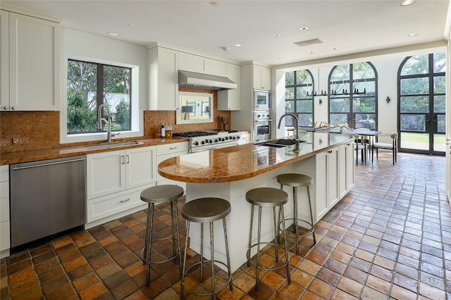 kitchen with backsplash, stainless steel appliances, sink, a center island with sink, and a breakfast bar