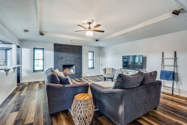 living room with ceiling fan, dark hardwood / wood-style floors, a textured ceiling, and a brick fireplace