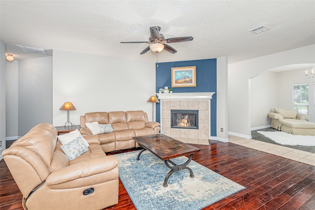 living room featuring hardwood / wood-style floors, ceiling fan with notable chandelier, a fireplace, and a textured ceiling