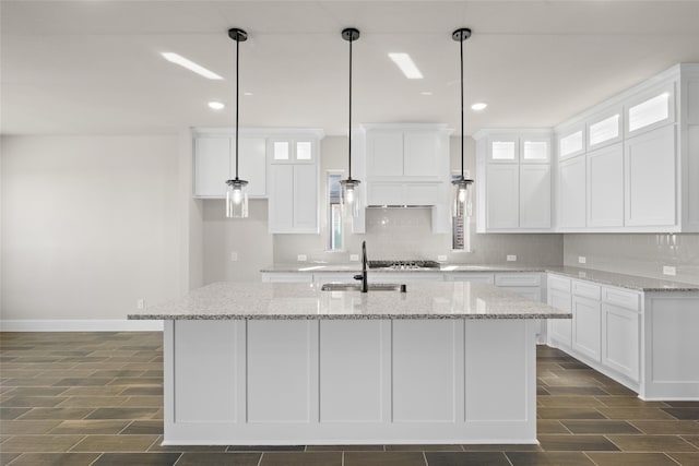 kitchen featuring a kitchen island with sink, white cabinetry, and light stone countertops